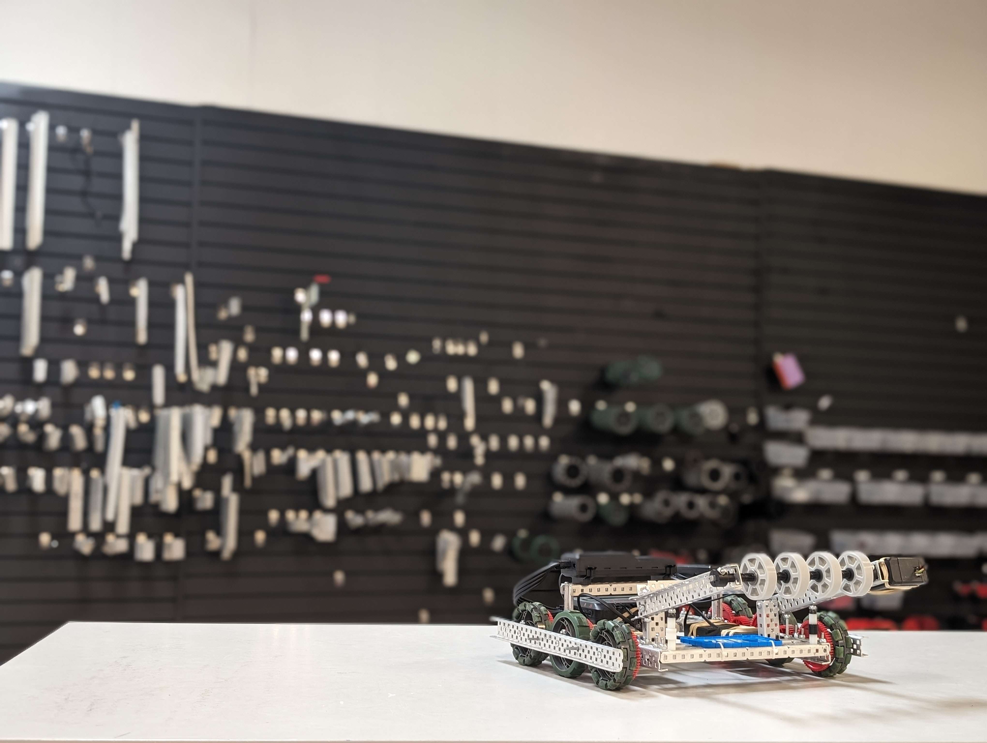 A VEX V5 robot on the workbench in front of the parts wall